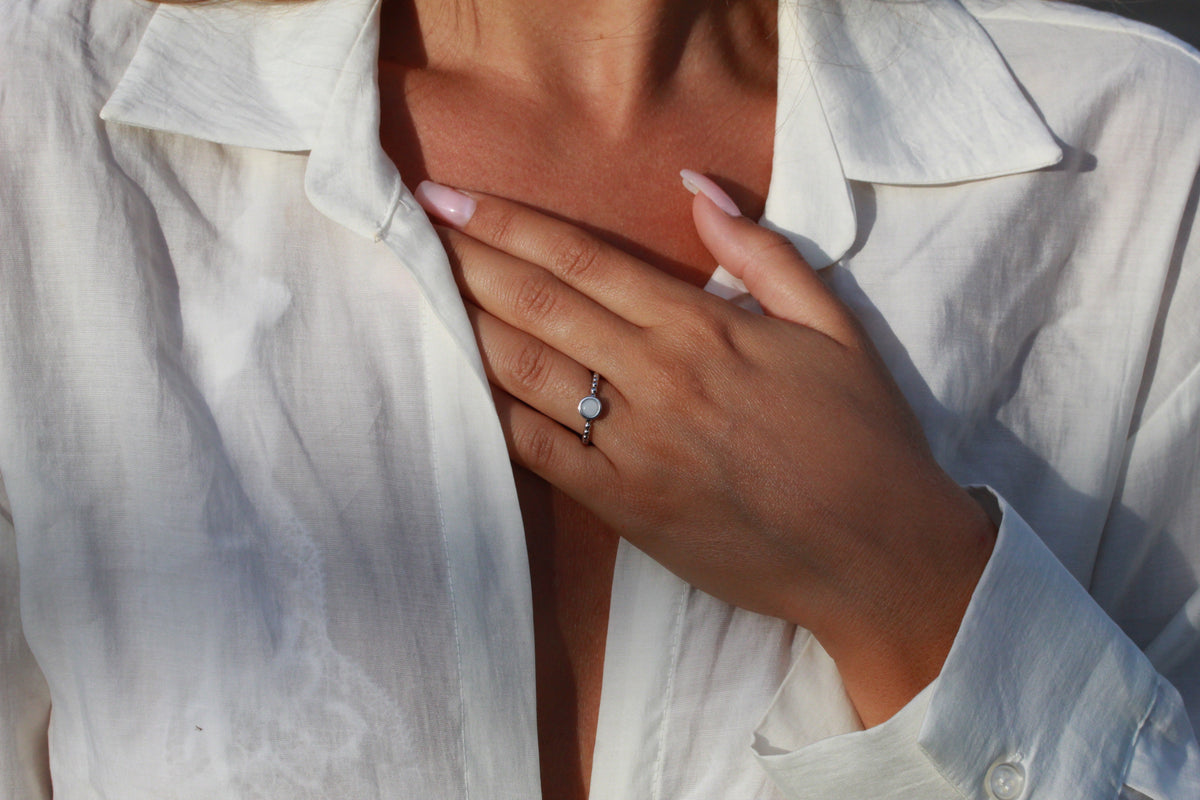 Massief witgouden ring met een ronde moedermelkhars en een kleine zirkonia, gedragen door een persoon met een witte blouse.