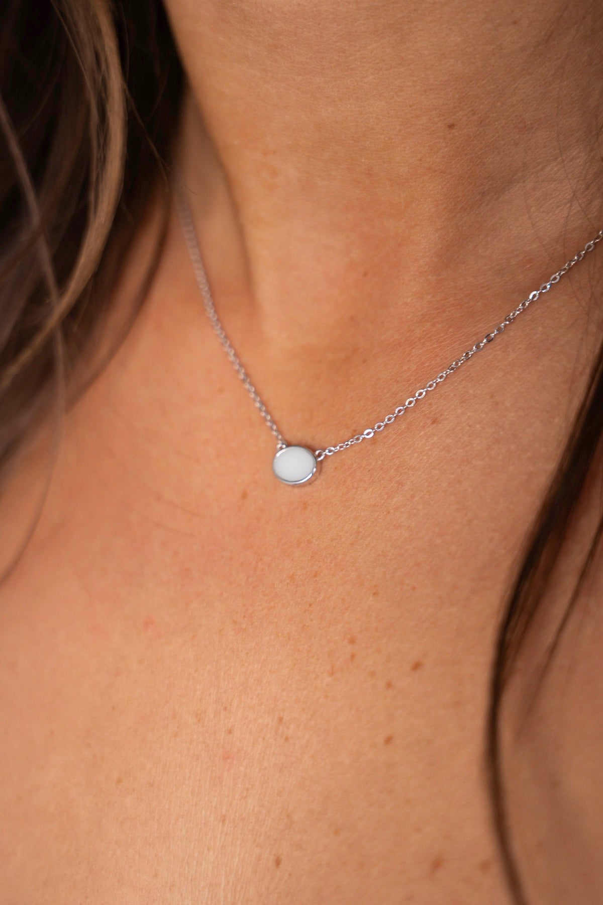 Close-up van de Juna moedermelkketting van massief witgoud met geslepen schakels en een glad ovaal steentje.
