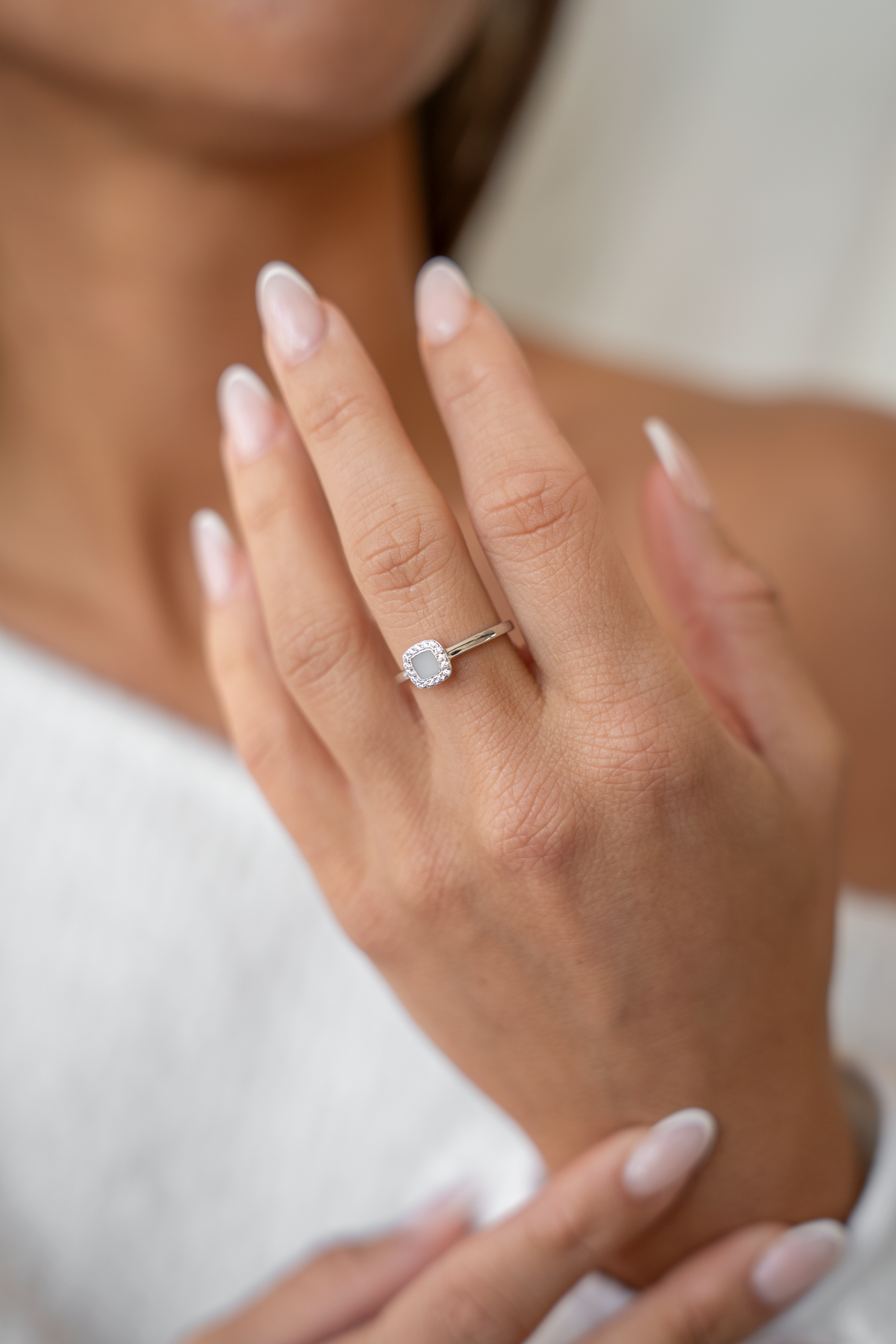 Massief witgouden ring met een ovale moedermelkhars steen, omringd door kleine zirkonia's, gedragen aan een hand met verzorgde nagels.
