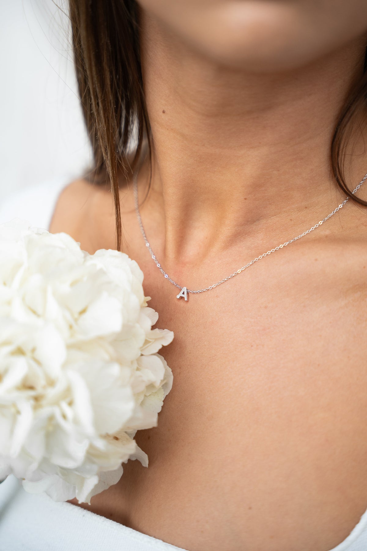 Zilveren ketting met een hangende letter 'A', gedragen door een persoon met een bloem in de hand.