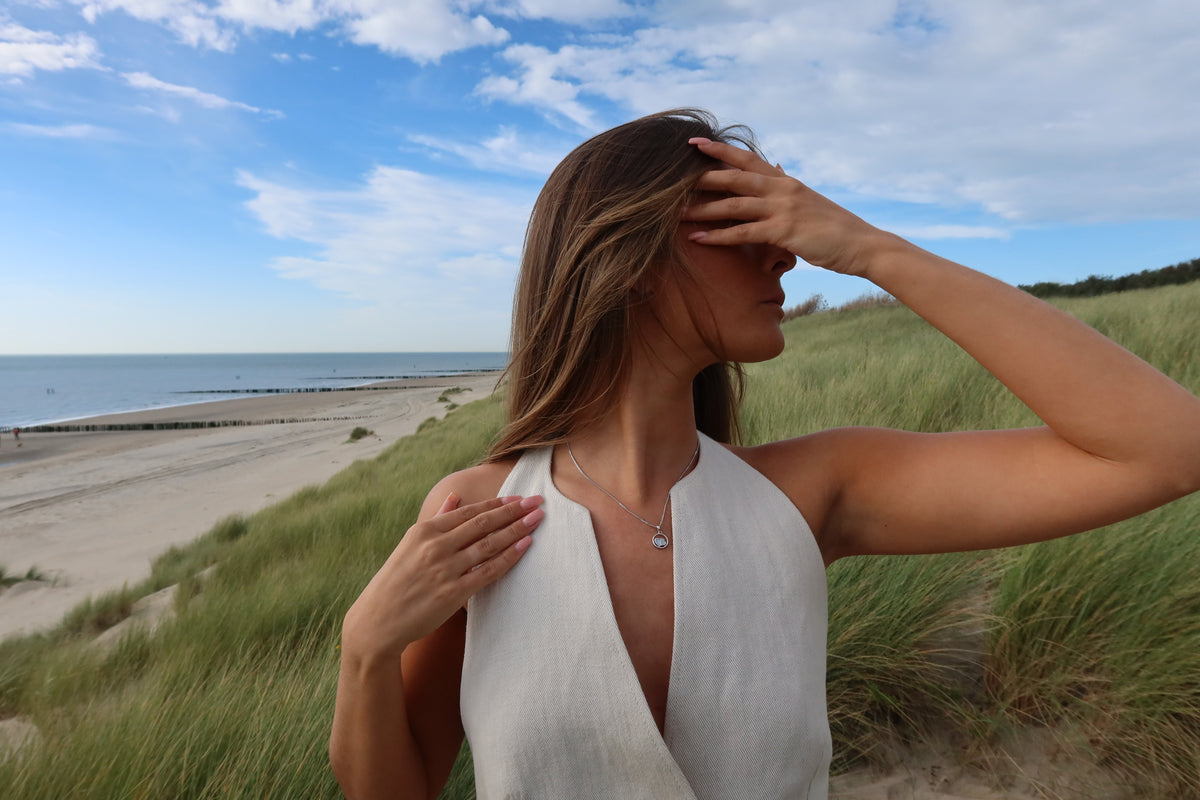 Hanger van 925 zilver met een subtiele afwerking, zichtbaar gedragen door een vrouw in een lichte outfit, met een strandachtige achtergrond.