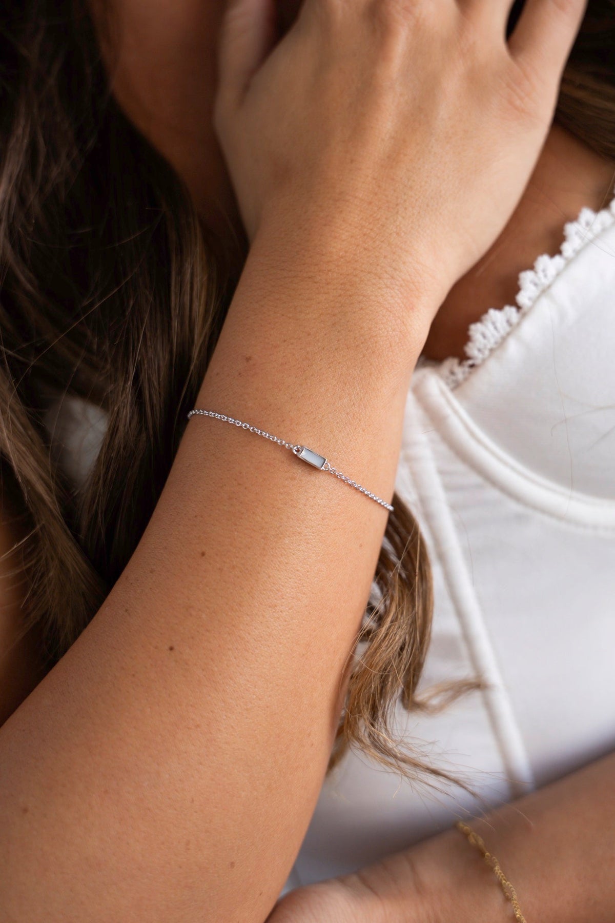Witgouden Britt-armband met rechthoekig moedermelksteentje om de pols, de hand in het haar.