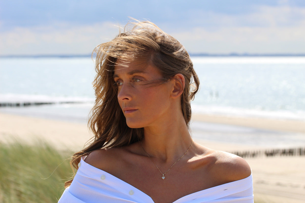 Hanger van massief roségoud met een druppelvormige moedermelkhars en een subtiele glans, gedragen door een vrouw met los haar aan het strand.
