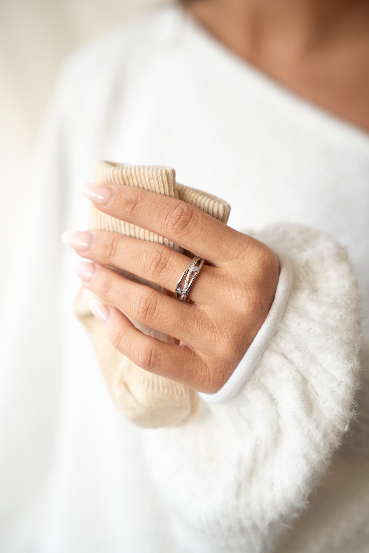 Massief witgouden ring met een subtiele band en een ingelegde steen van moedermelk, gedragen door een persoon met een lichte trui.