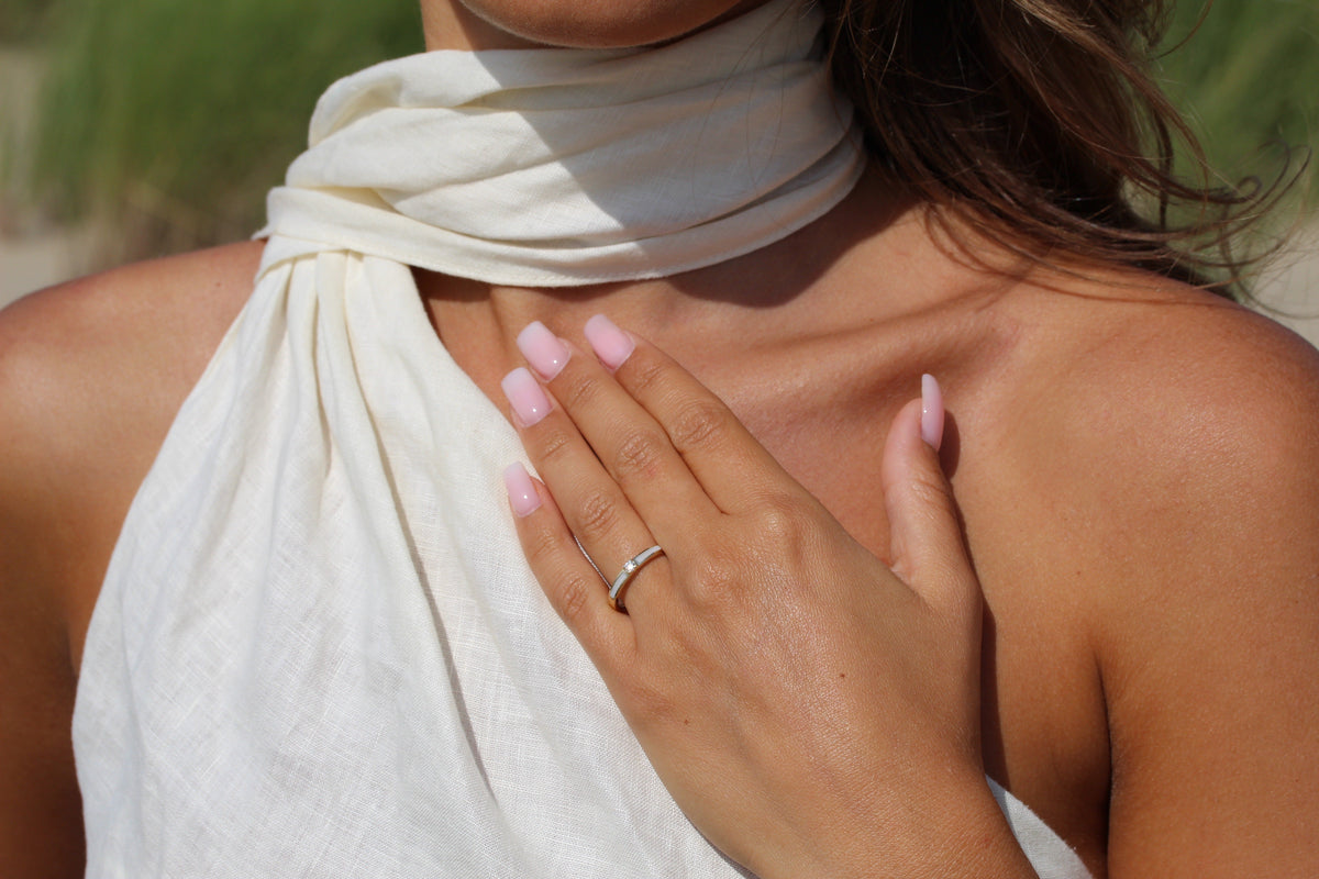 Massief witgouden ring met een gladde afwerking, gedragen door een persoon met een lichte huid en roze nagellak.