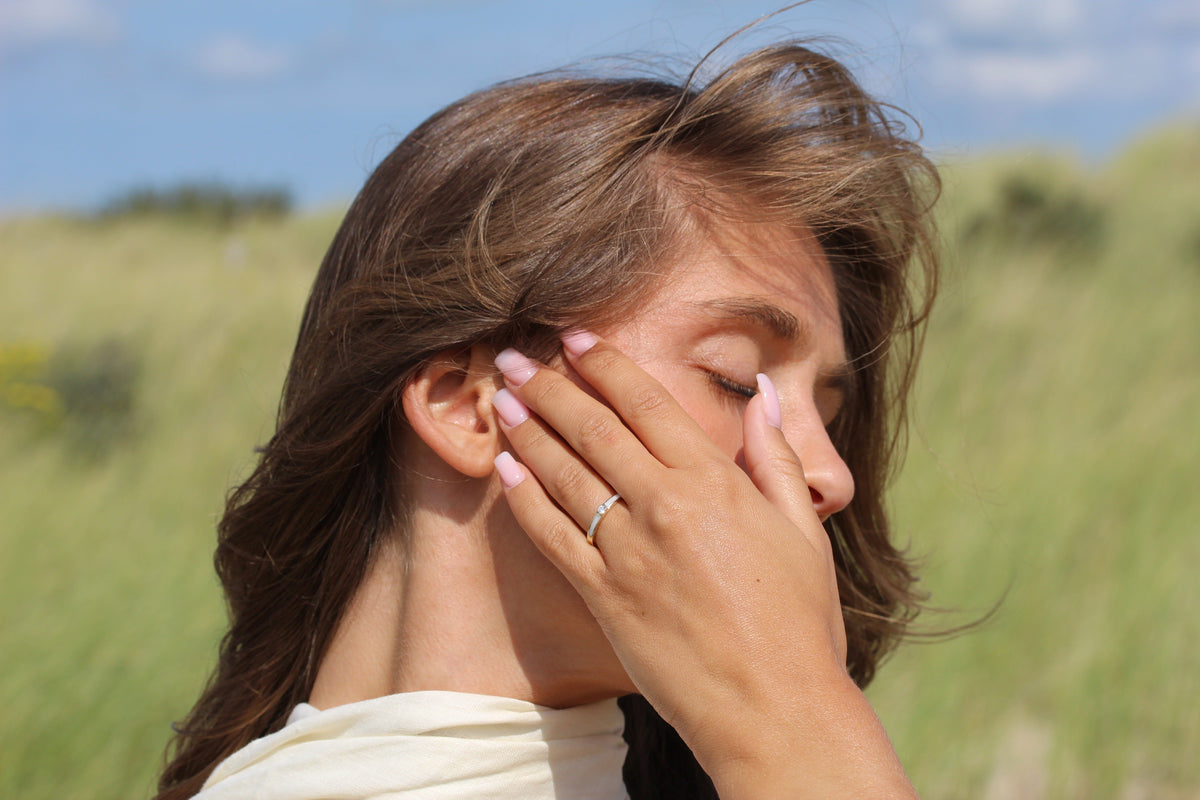 Dunne ring van massief witgoud met een subtiele afwerking, gedragen door een vrouw met een hand voor haar gezicht.