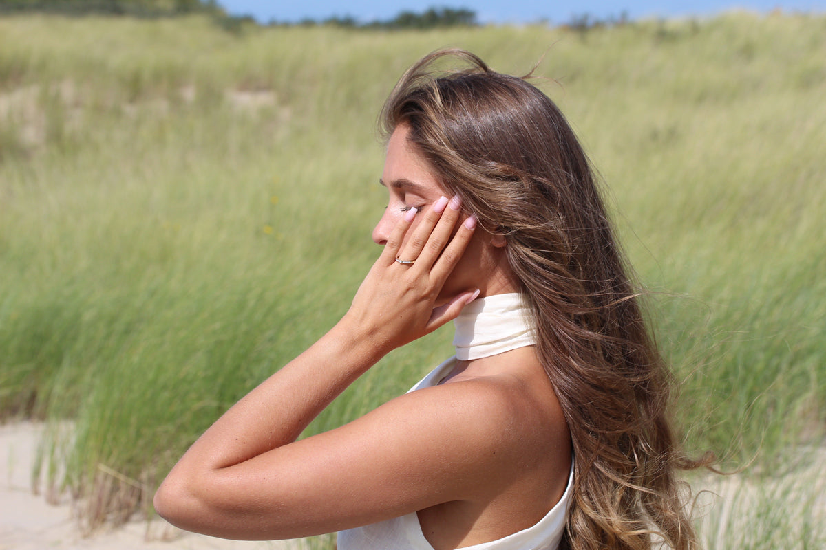Elegante moedermelk-ring in massief roségoud, gedragen door een vrouw met lang bruin haar, op een achtergrond van groene grasvelden.