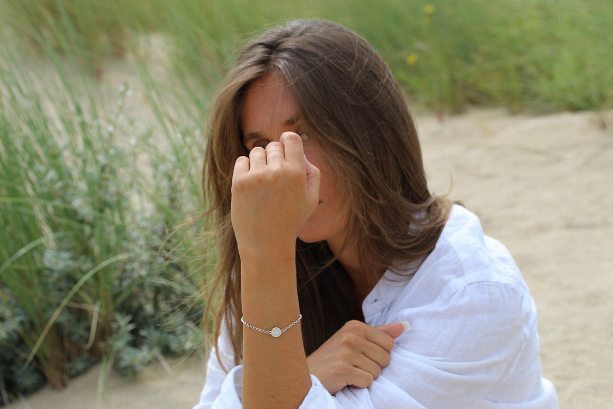Armband van 925 zilver met een ronde schijf waarin moedermelk is verwerkt, gedragen door een vrouw in een natuurlijke omgeving.