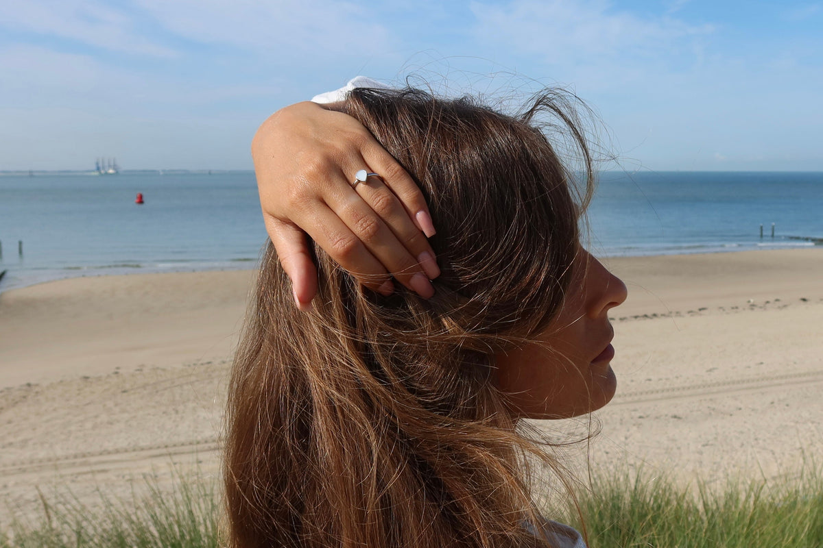 Moedermelk-ring in massief witgoud met een glanzende afwerking, gedragen door een vrouw aan het strand.
