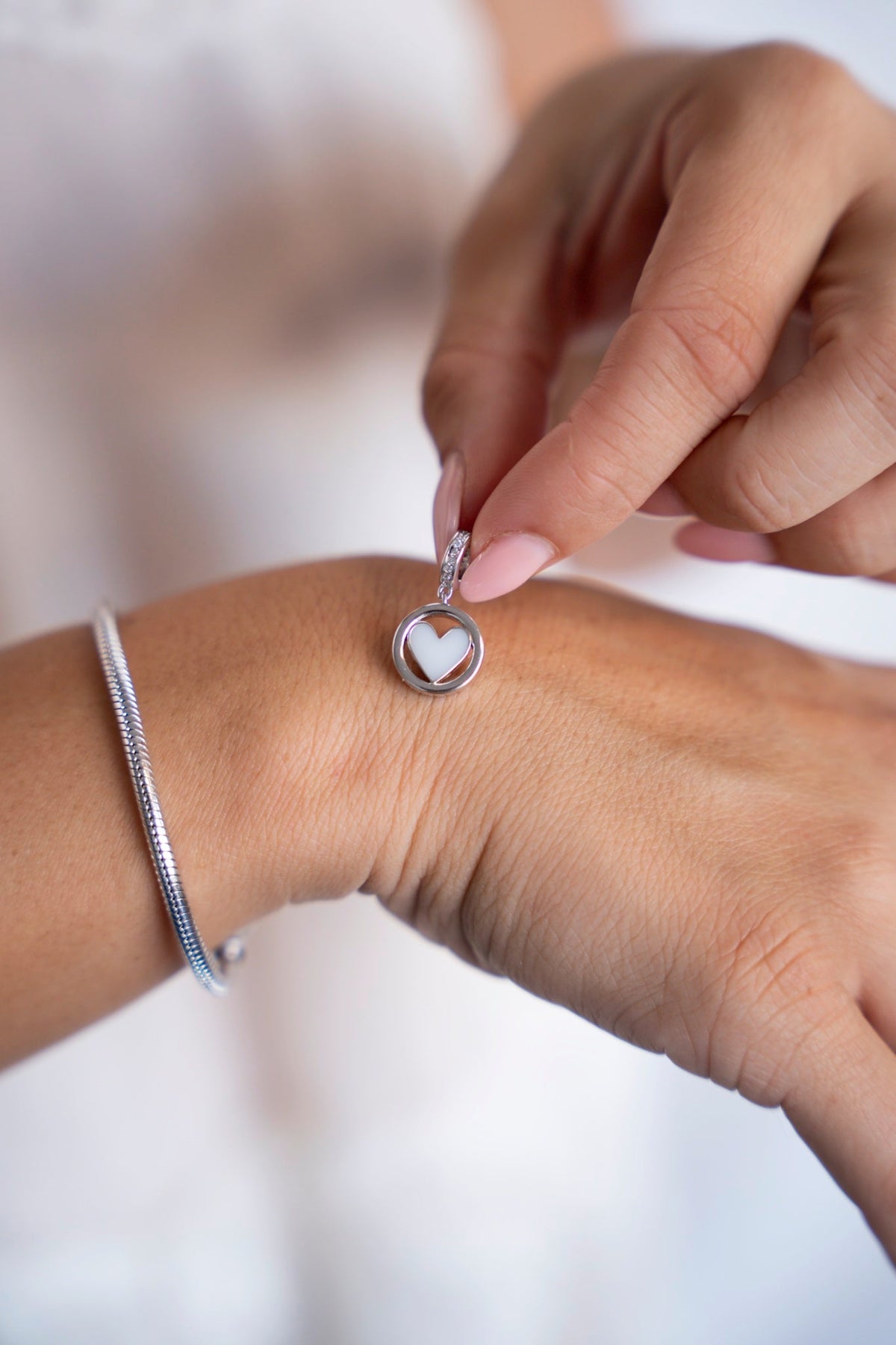 Eline moedermelkbedel van massief witgoud met hartvormige moedermelk in een rond kader, naast een armband.