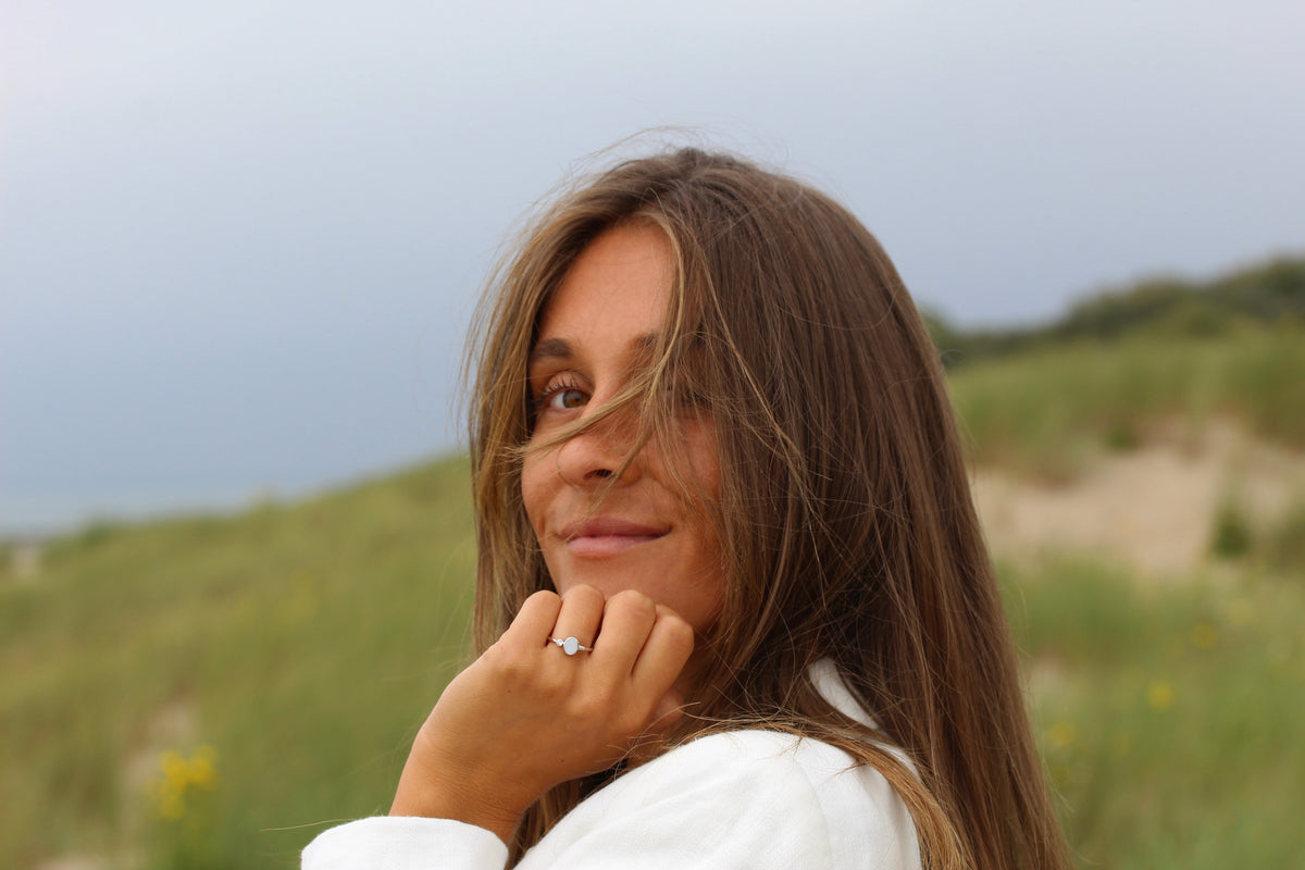 Massief geelgouden ring met een ingelegde steen van moedermelk, gedragen door een vrouw met lang bruin haar in een natuurlijke omgeving.