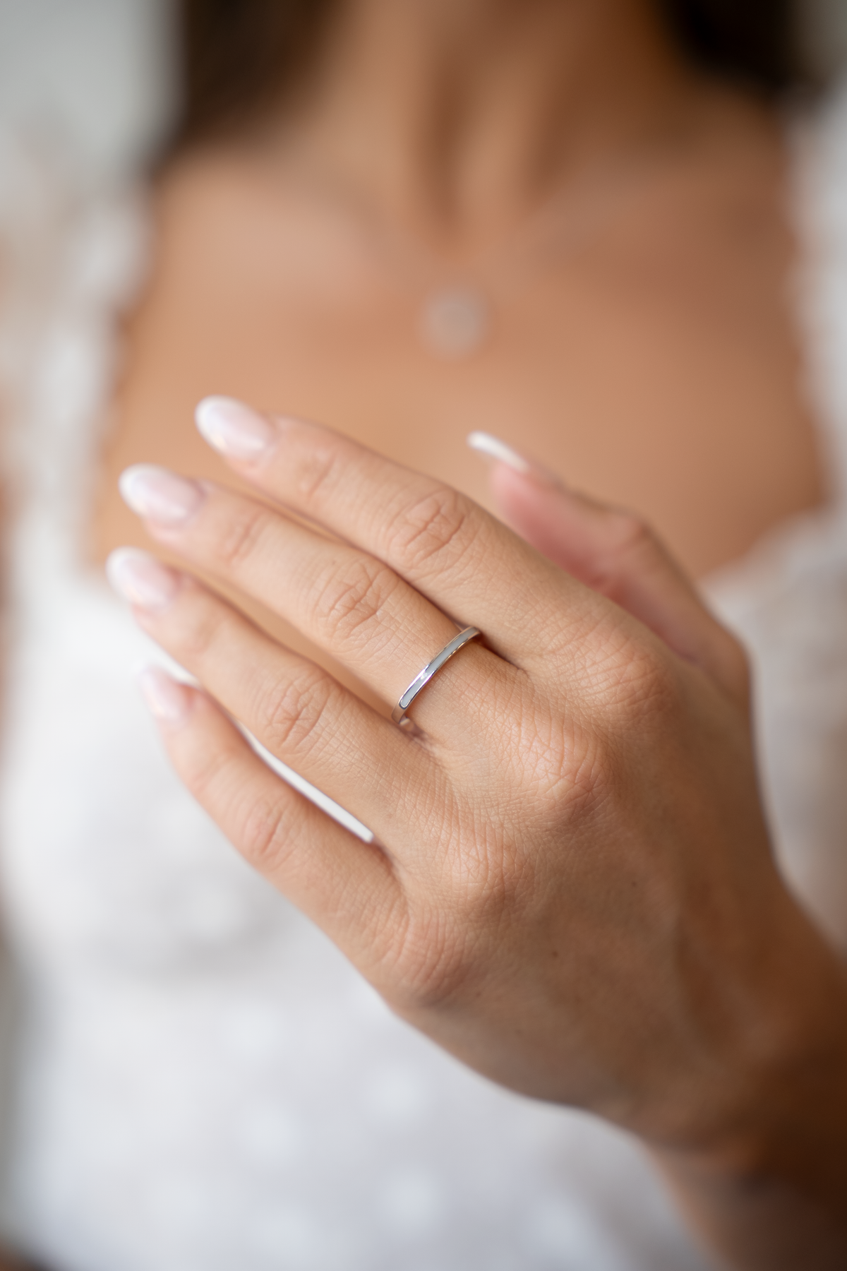 Dunne ring van massief witgoud met een subtiele, glanzende afwerking, gedragen aan de hand van een persoon.