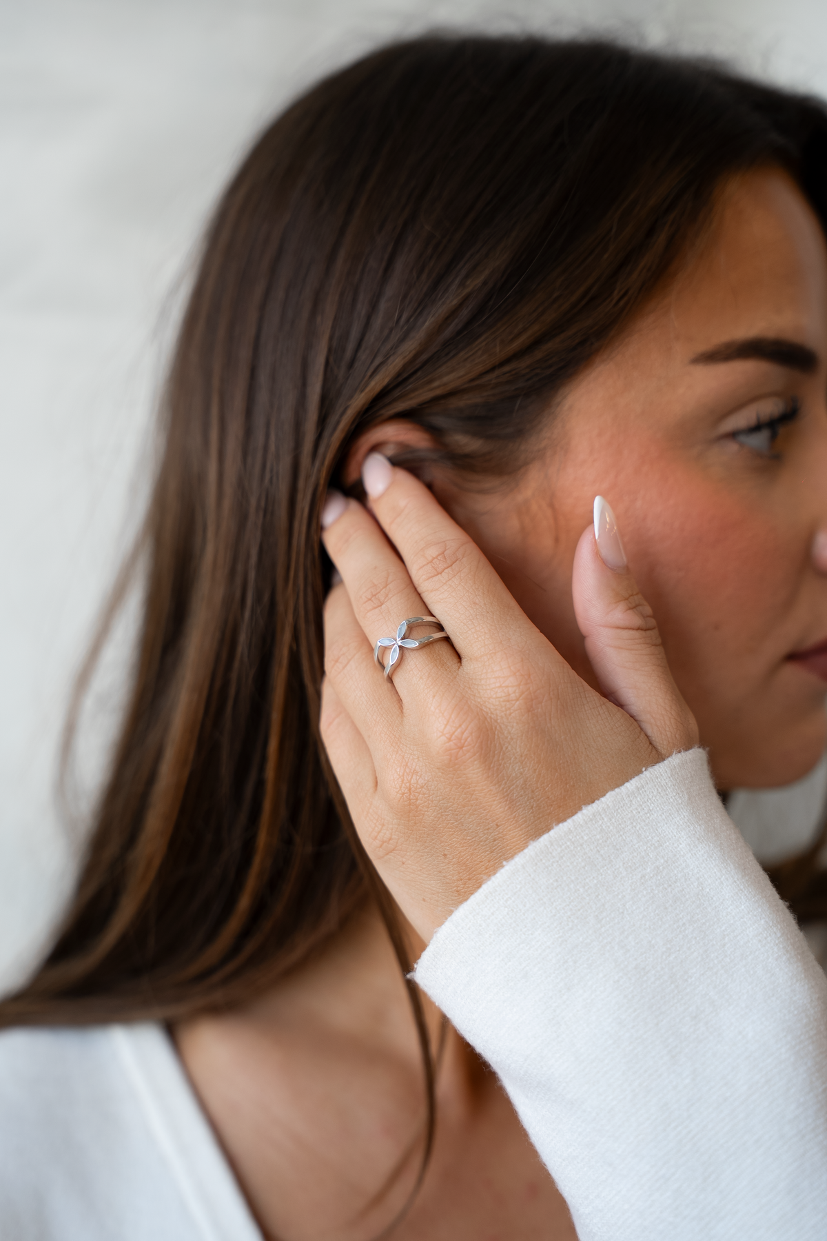 Moedermelk-ring van massief witgoud met een elegante bloemvorm, gedragen door een persoon met bruin haar.