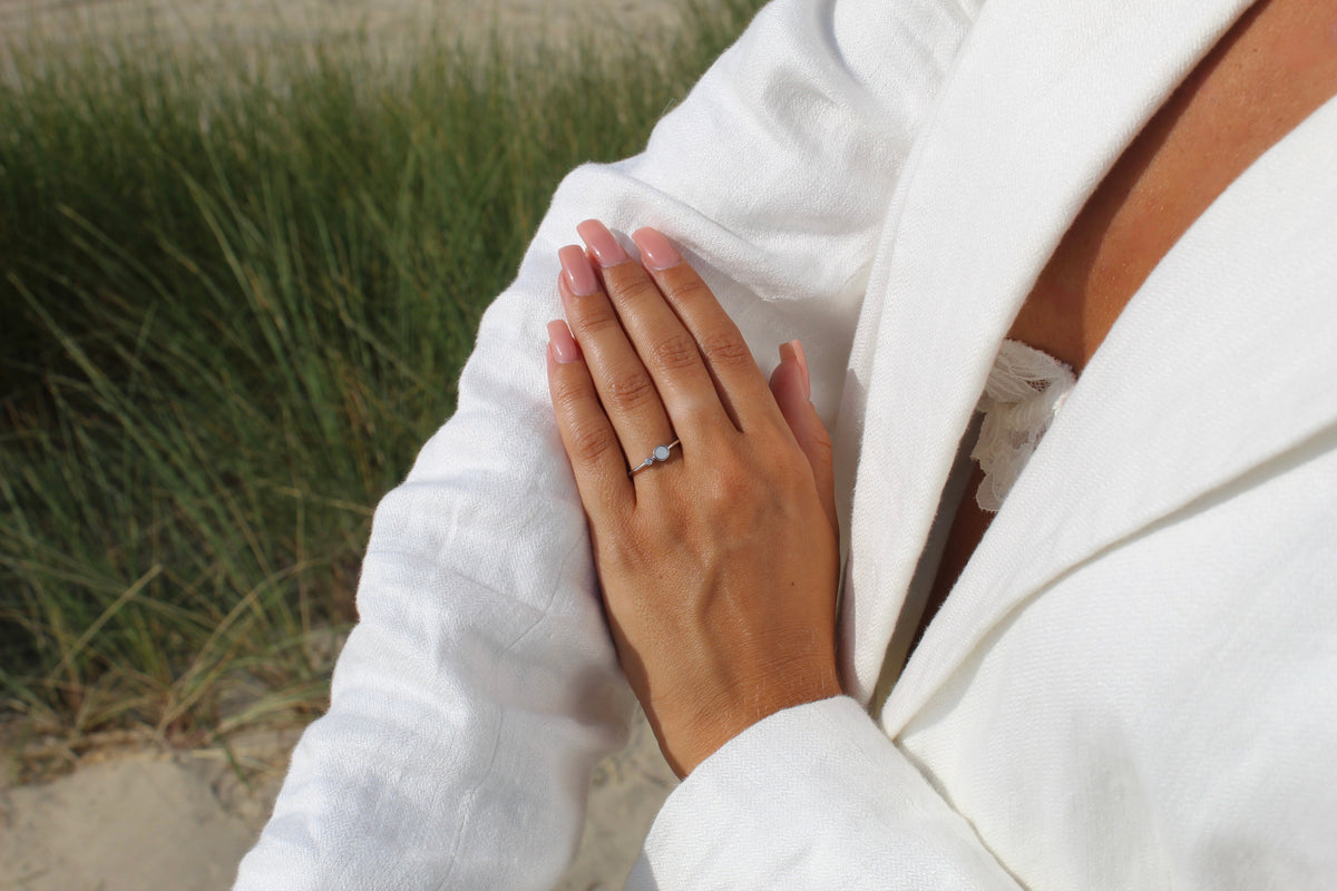Massief witgouden ring met een heldere zirkonia, gedragen door een persoon met een witte blazer en een natuurlijke achtergrond.