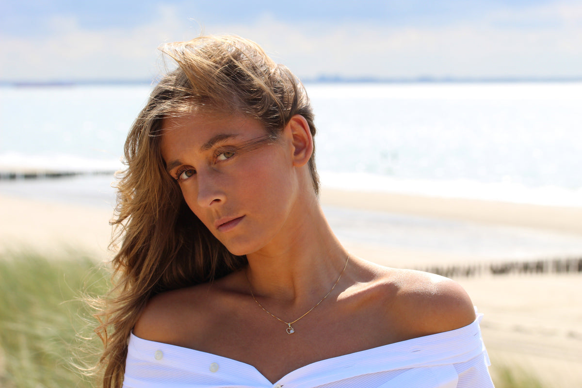 Hanger van 925 zilver in de vorm van een hart, met een transparante moedermelkhars en een subtiele glans, gedragen door een vrouw met een off-shoulder blouse.