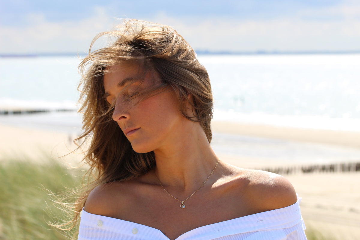 Hanger van 925 zilver in de vorm van een hart, met een transparante moedermelkhars en een subtiele glans, gedragen door een vrouw met loshangend haar.