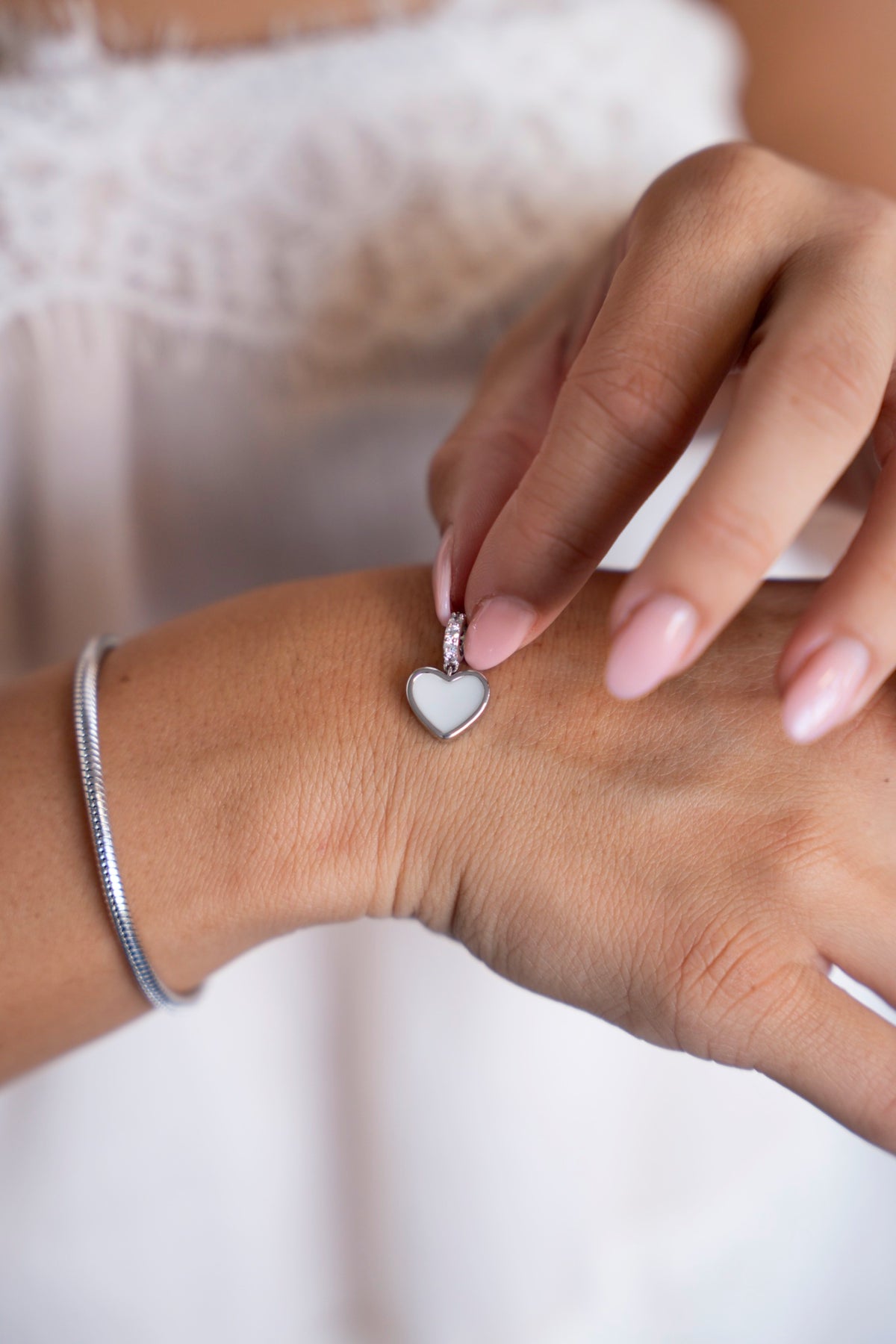 Indy moedermelkbedel van zilver vastgehouden boven de hand, naast een zilveren armband.