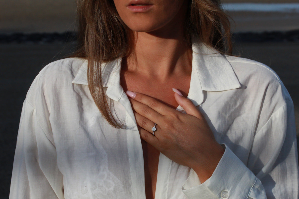 Massief roségouden ring met een ronde moedermelkharssteen, gedragen door een vrouw met een witte blouse.