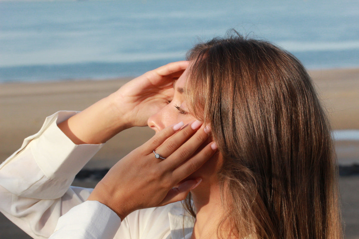Massief roségouden moedermelkring met een eenvoudige, elegante vorm, gedragen door een persoon met bruin haar aan het strand.