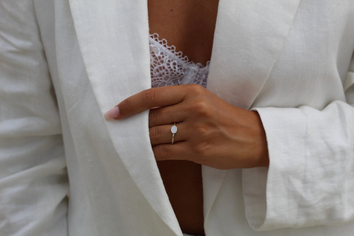 Ring van 925 zilver met een ovale moedermelkhars in het midden, gedragen door een persoon met een witte blazer.