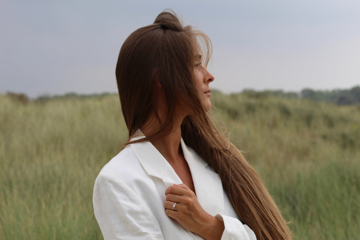 Massief gouden ring met een heldere steen van moedermelk, gedragen door een vrouw met lang bruin haar, in een natuurlijke omgeving.