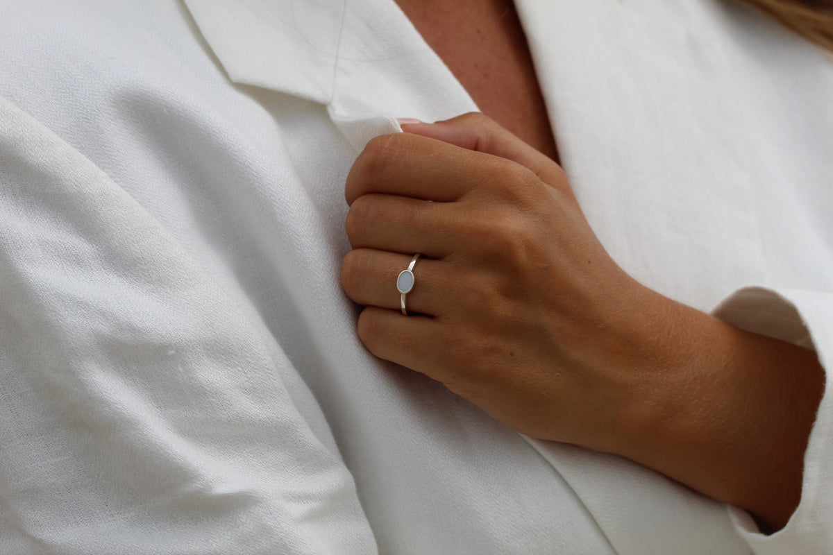 Massief geelgouden ring met een ovaal vlak van moedermelkhars, gedragen op een hand met een witte blouse.