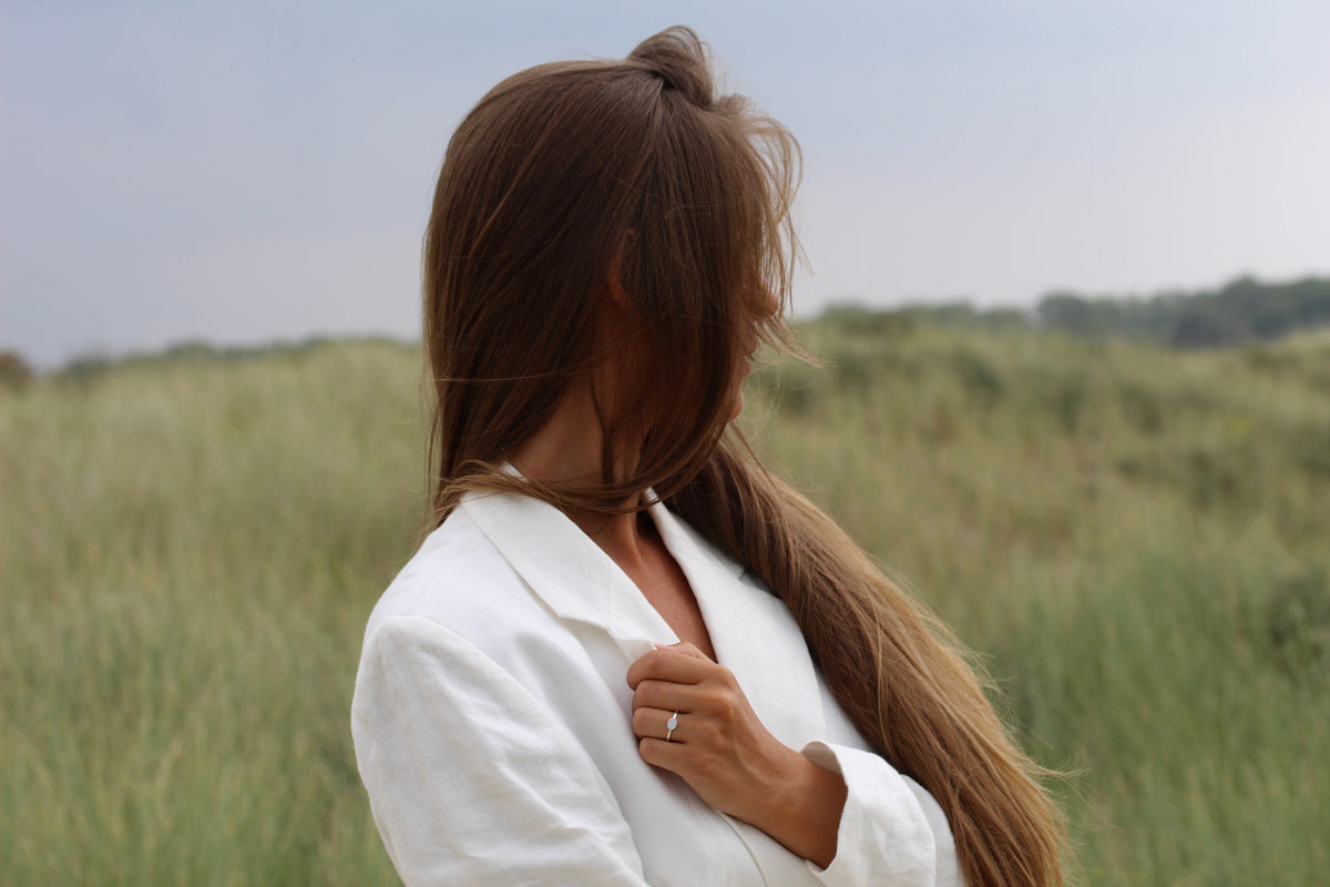 Massief roségouden ring met een heldere zirkonia, gedragen door een vrouw met lang bruin haar in een groene omgeving.