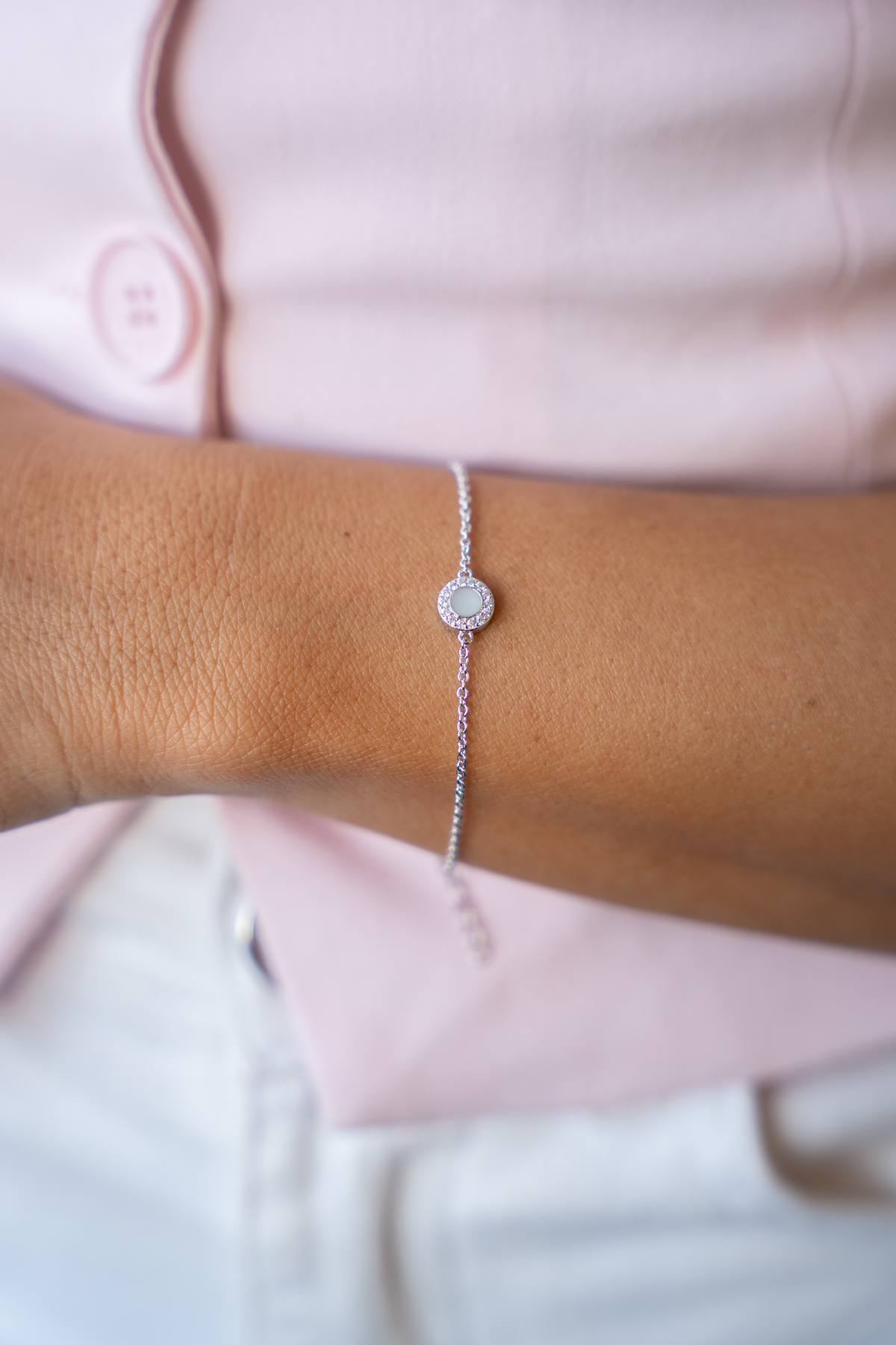 Armband van massief witgoud met een ronde schijf van moedermelkhars en een zirkonia rand, gedragen om een pols.