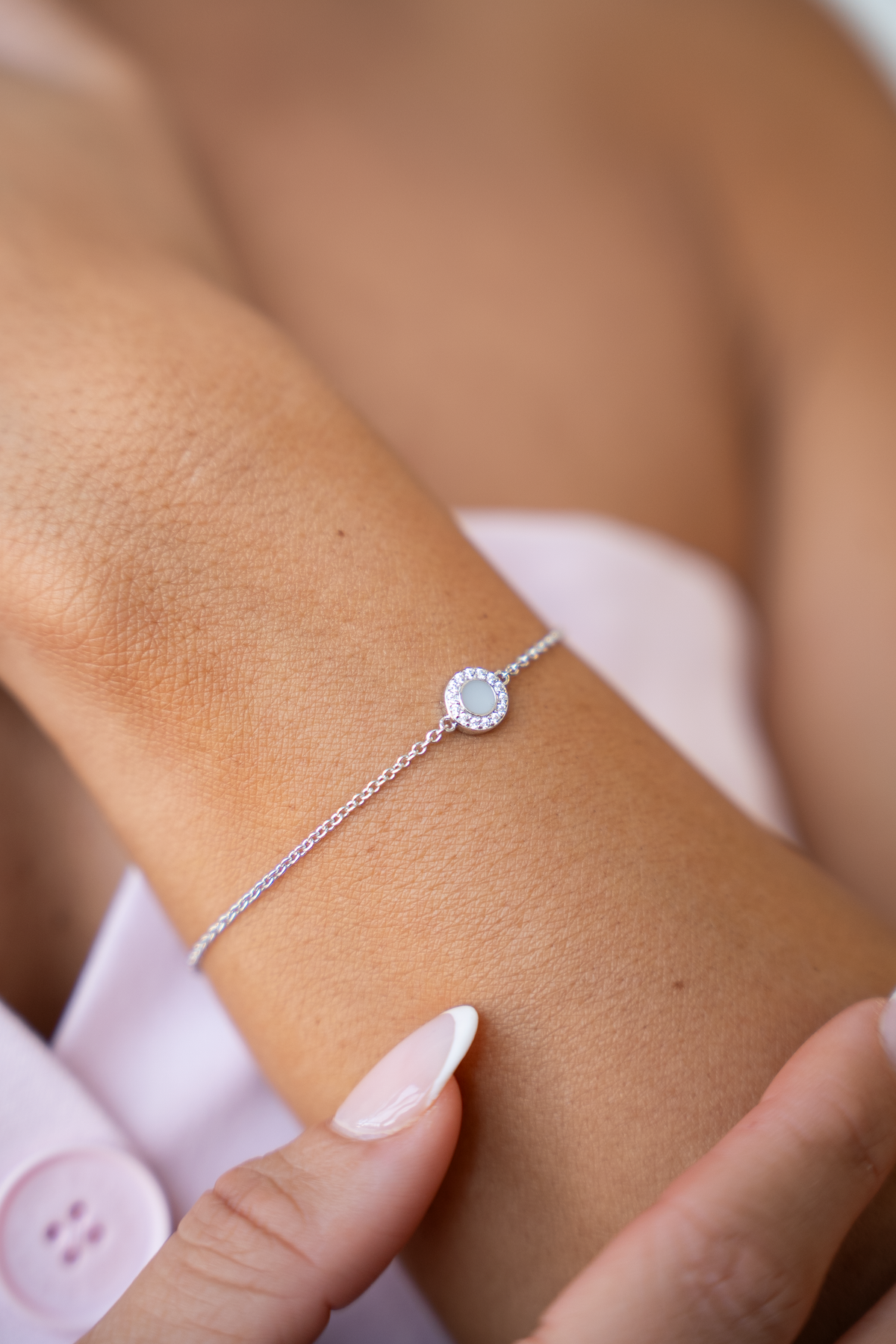 Armband van massief witgoud met een ronde schijf van moedermelkhars, omringd door zirkonia, gedragen om een pols.