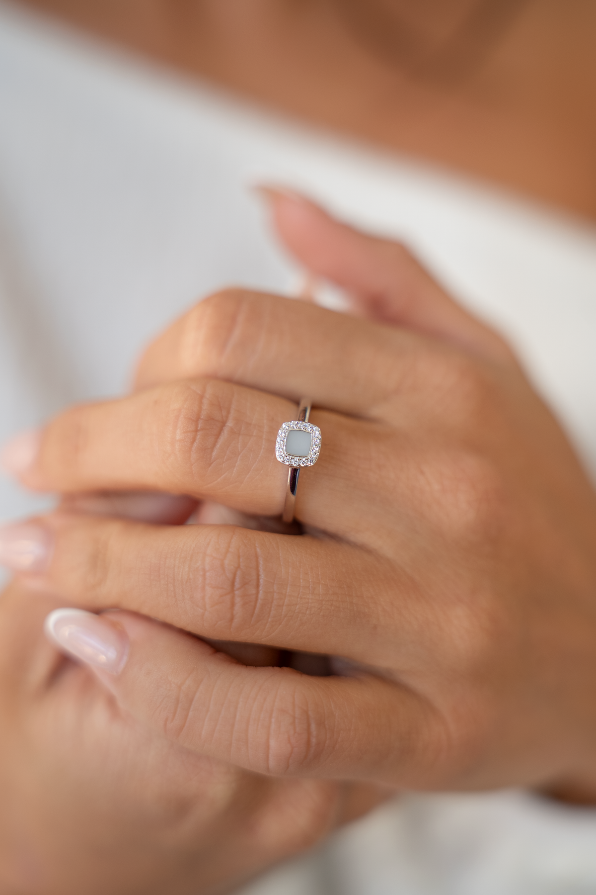 Massief witgouden ring met een vierkante zirkonia omringd door kleine steentjes, gedragen op een hand met verzorgde nagels.