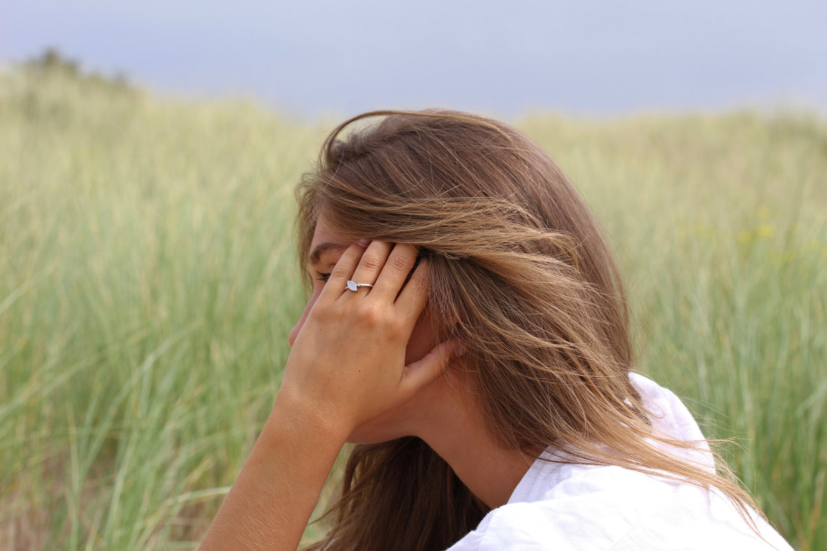 Massief roségouden ring met een heldere zirkonia, gedragen door een vrouw met lang, bruin haar, in een groene omgeving.