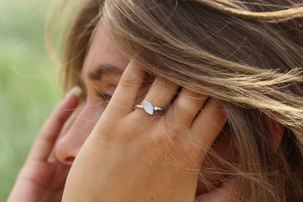 Massief witgouden ring met een ovaal moedermelkhars en kleine zirkonia's, gedragen door een persoon met los haar.