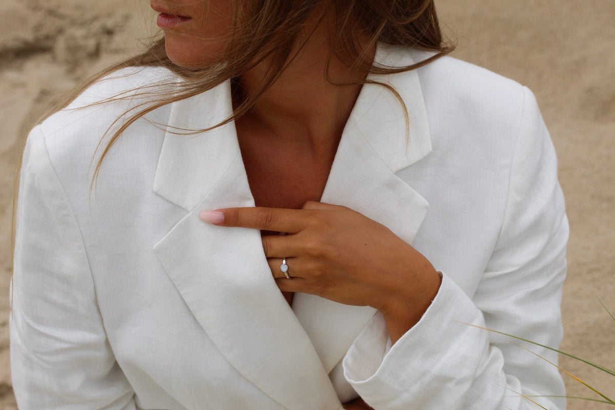 Moedermelkring van massief witgoud met een heldere zirkonia, gedragen door een vrouw in een witte blazer.