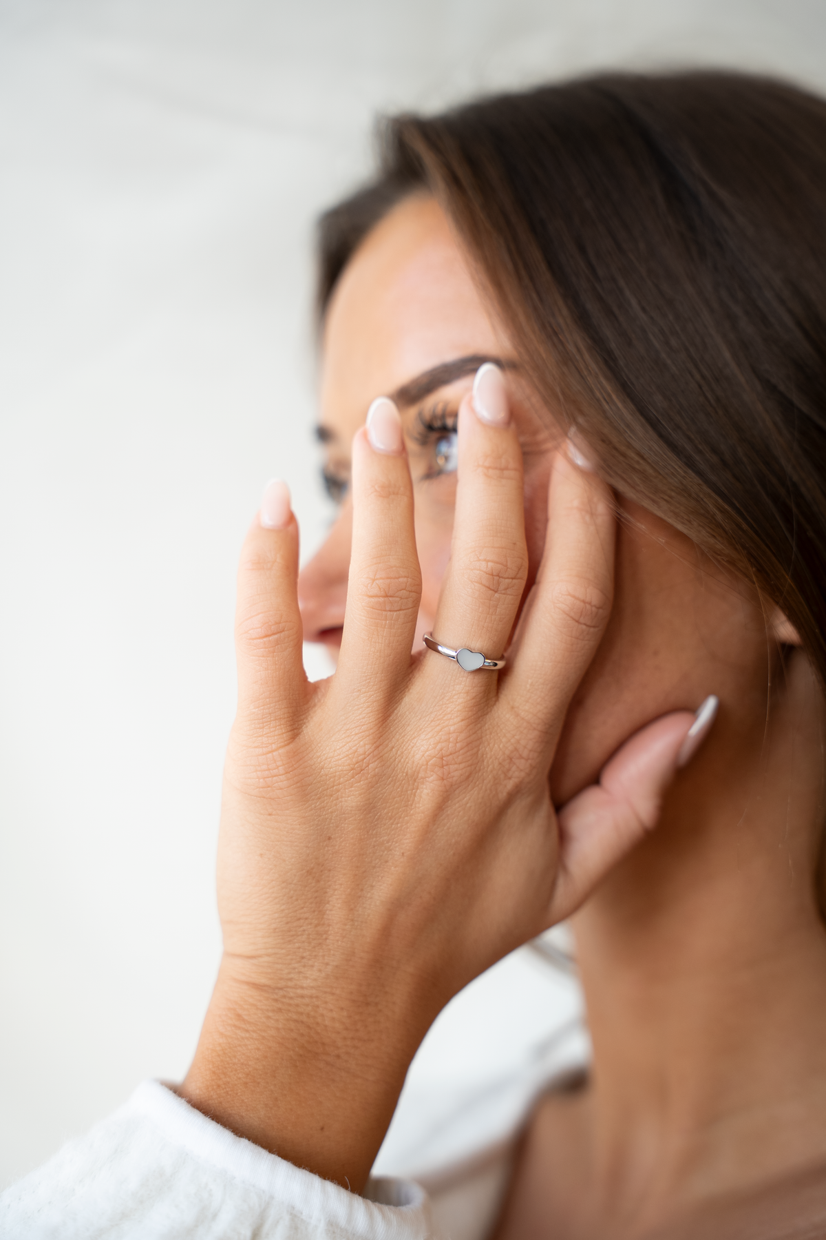 Moedermelk-ring van 925 zilver met een subtiele, ronde steen van moedermelk, gedragen door een vrouw die haar hand tegen haar gezicht houdt.