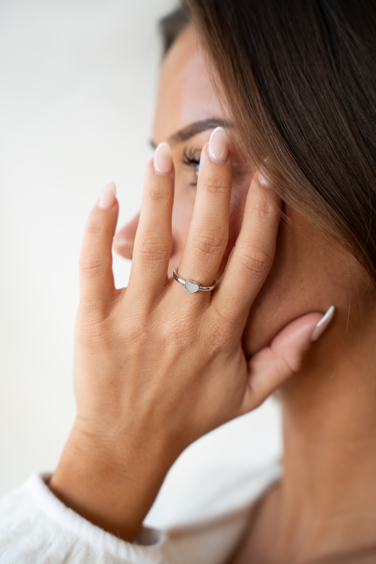 Dunne ring van massief witgoud met een ovaal vlak van moedermelkhars, gedragen door een persoon met een hand voor het gezicht.