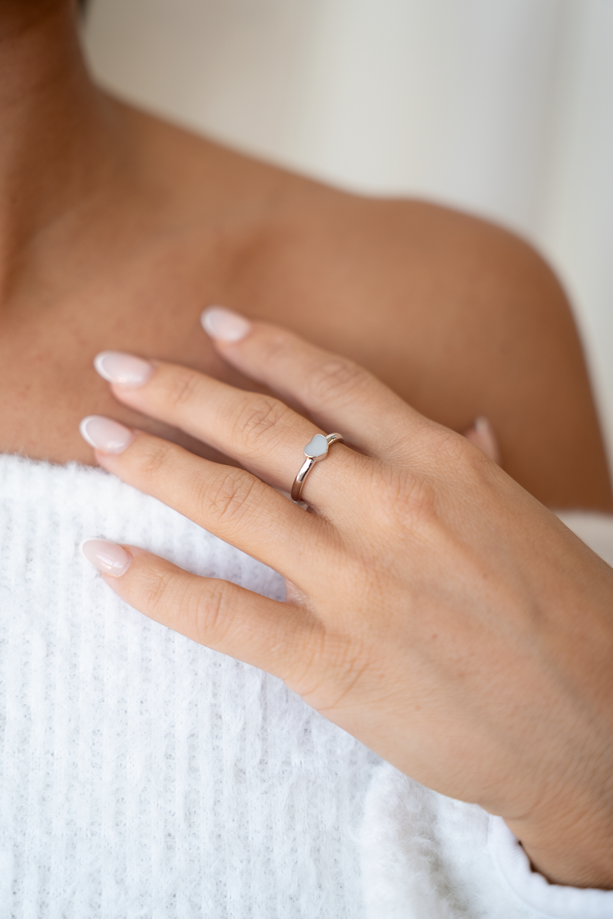 Ring van massief witgoud met een hartvormige moedermelkhars, gedragen op een hand met verzorgde nagels.