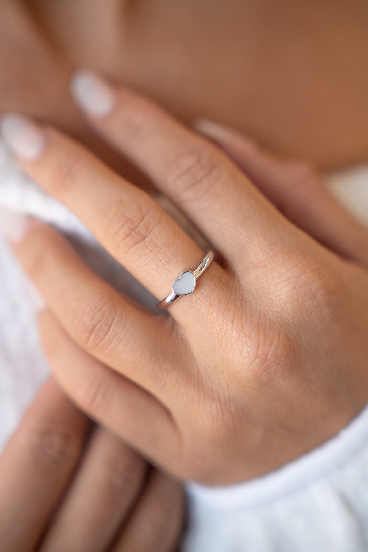 Ring van massief witgoud met een hartvormige moedermelkhars inlay, gedragen op een hand met natuurlijke nagels.