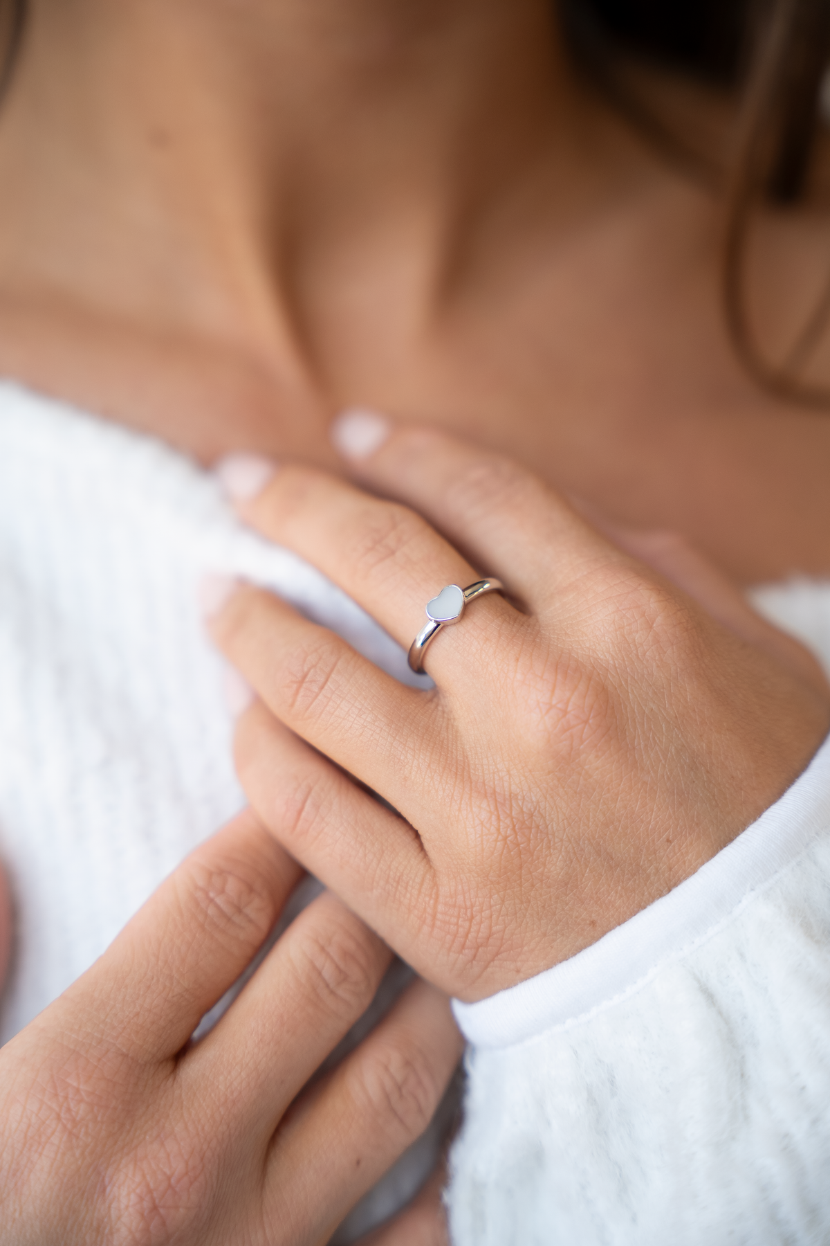 Ring van massief witgoud met een hartvormige moedermelkhars inleg, gedragen door een persoon met een witte trui.
