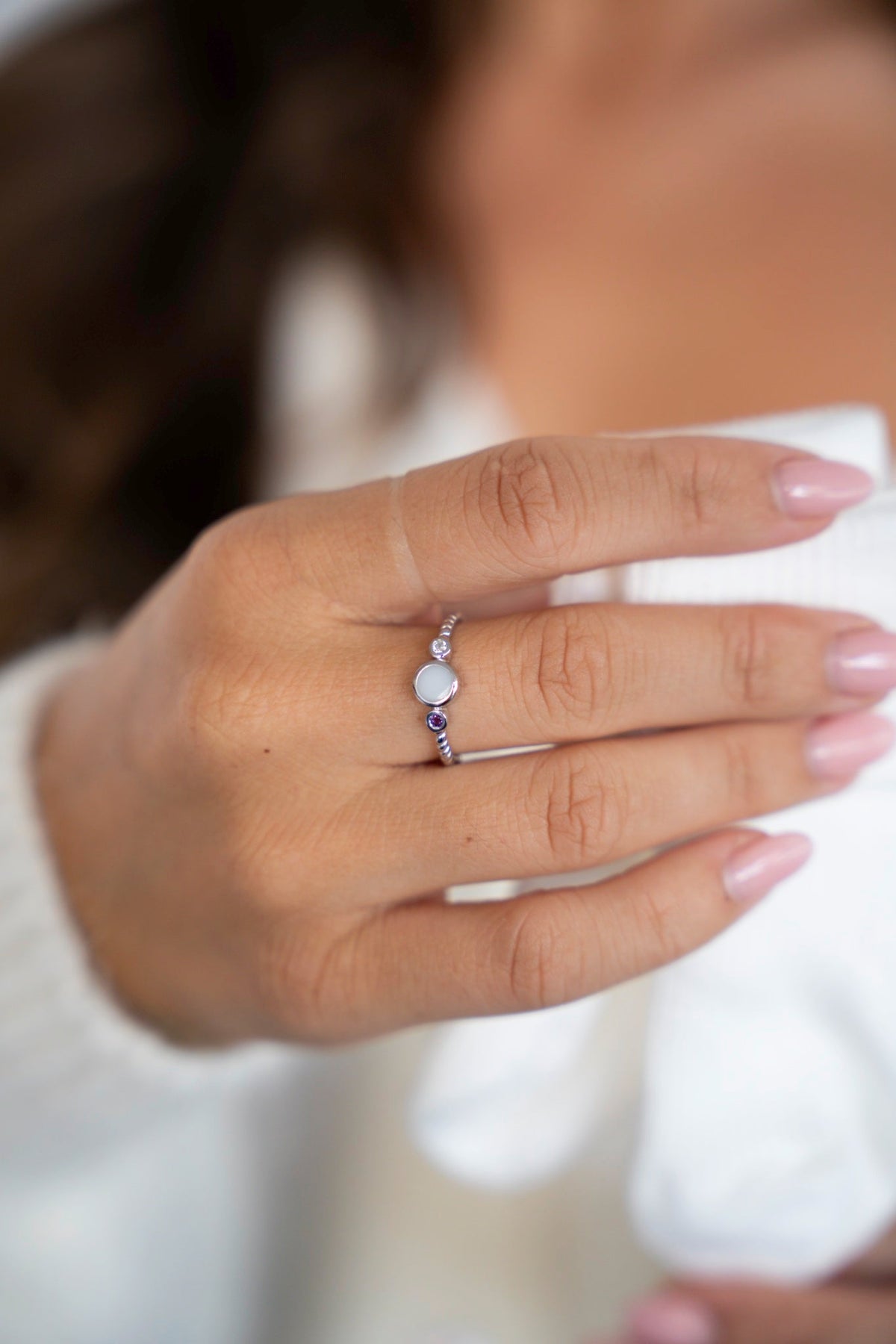 Witgouden Lot-ring met rond moedermelksteentje tussen twee geboortesteentjes, aan de hand voor een witte trui.