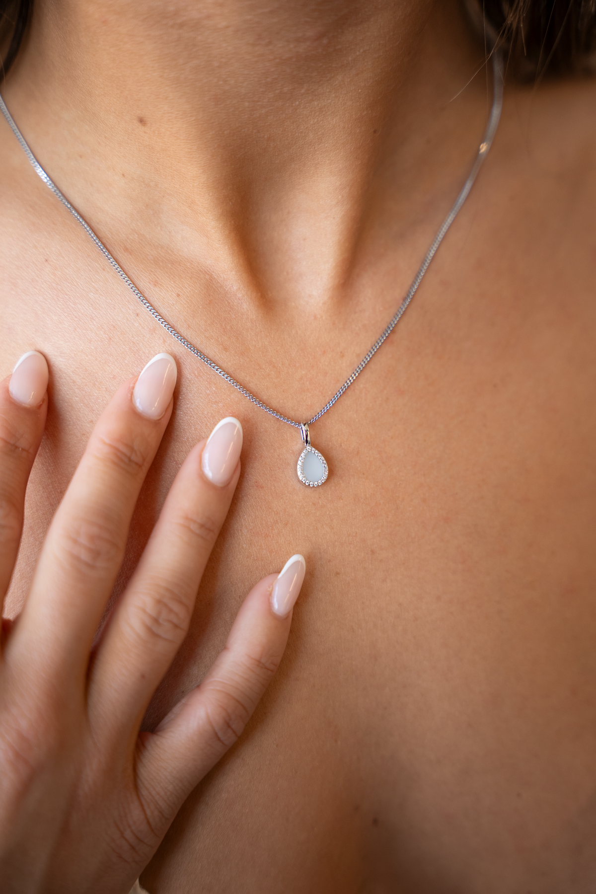 Hanger in witgoud met een druppelvormige moedermelkhars, omringd door kleine zirkonia's, gedragen door een persoon.