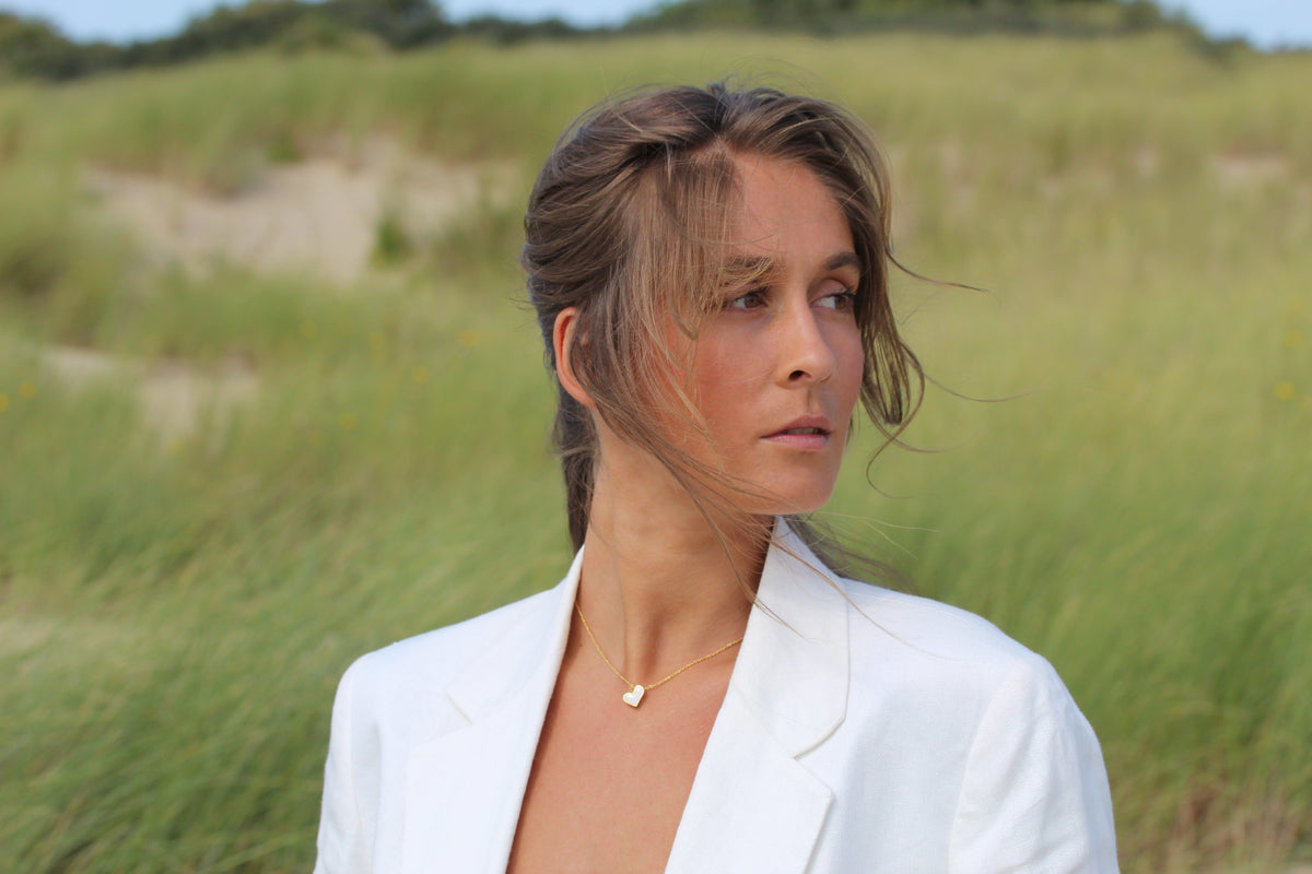 Hanger van massief geelgoud met een hartvormige moedermelkhars, gedragen door een vrouw in een witte blazer, met een groene achtergrond.