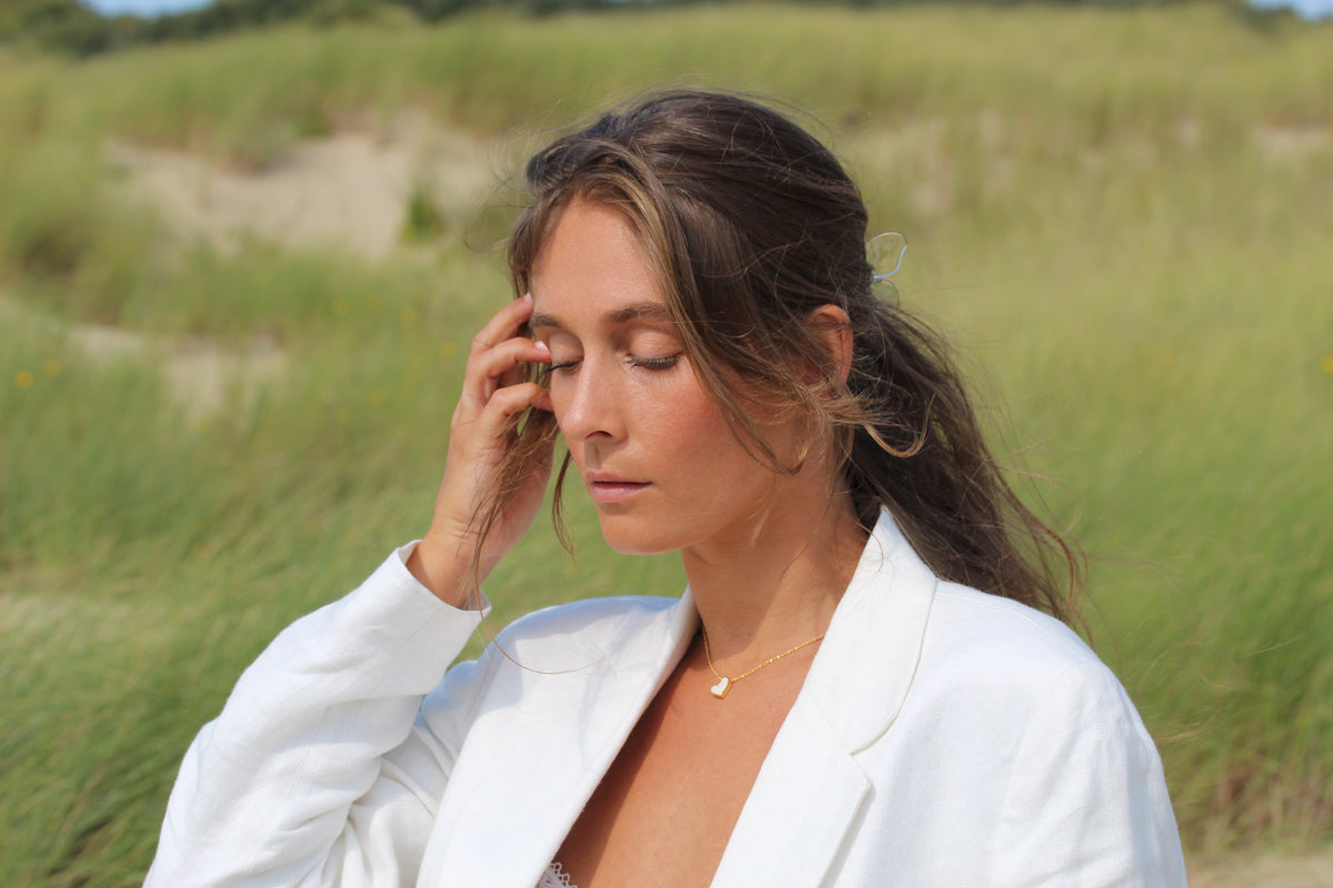 Ketting van massief roségoud met een hangende druppelvormige moedermelkhars en een subtiele glans, gedragen door een vrouw in een witte blazer.