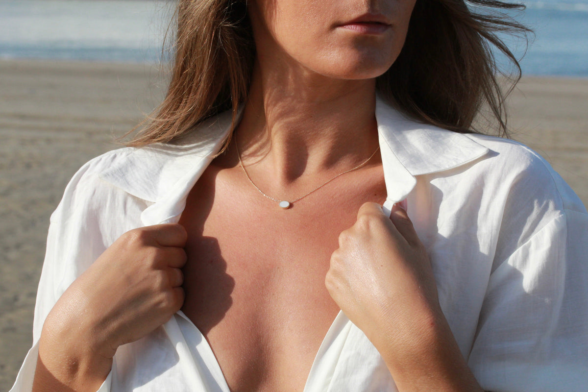 Hanger van massief goud met een gladde, ovale moedermelkhars in het midden, gedragen door een vrouw op het strand.