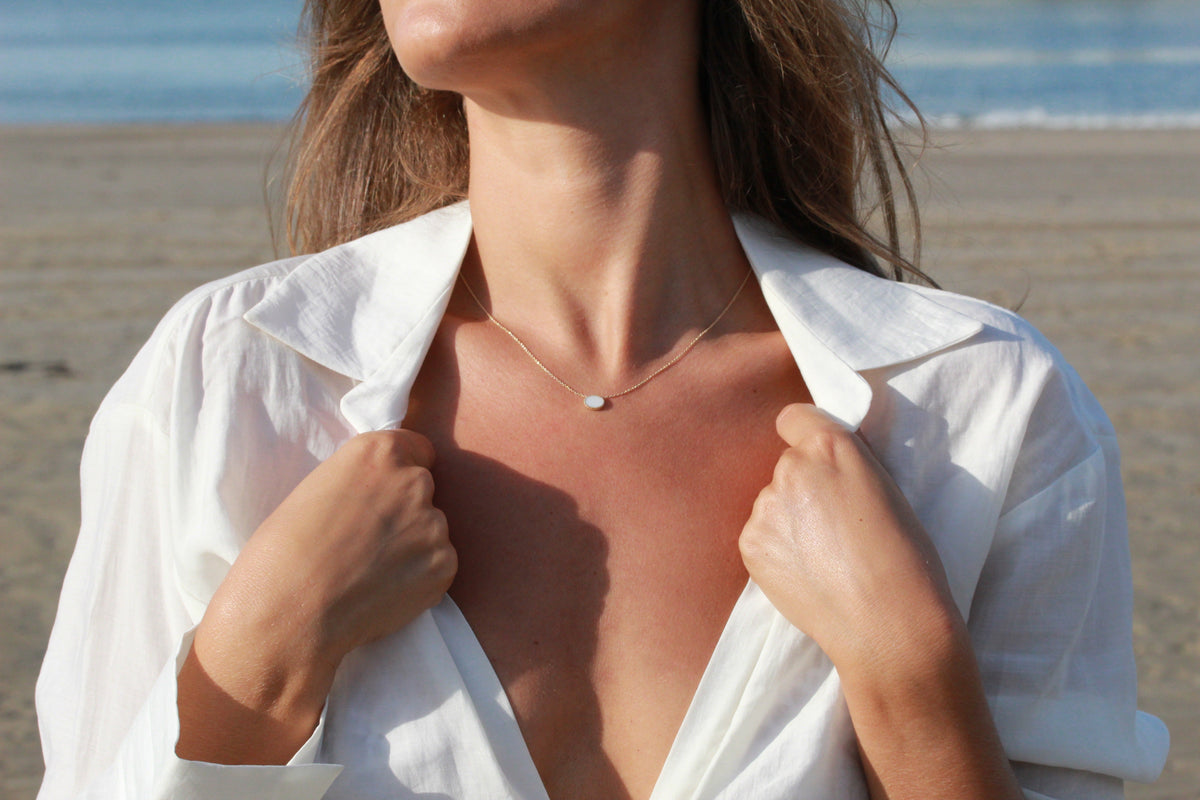 Massief roségouden ketting met een eenvoudige hanger van moedermelkhars, gedragen door een vrouw op het strand.