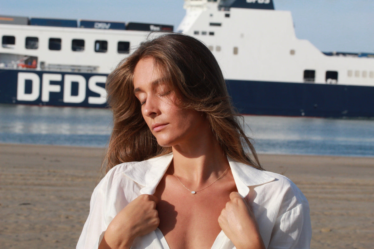 Ketting van massief witgoud met een subtiele hanger van moedermelkhars, gedragen door een vrouw met een natuurlijke uitstraling.
