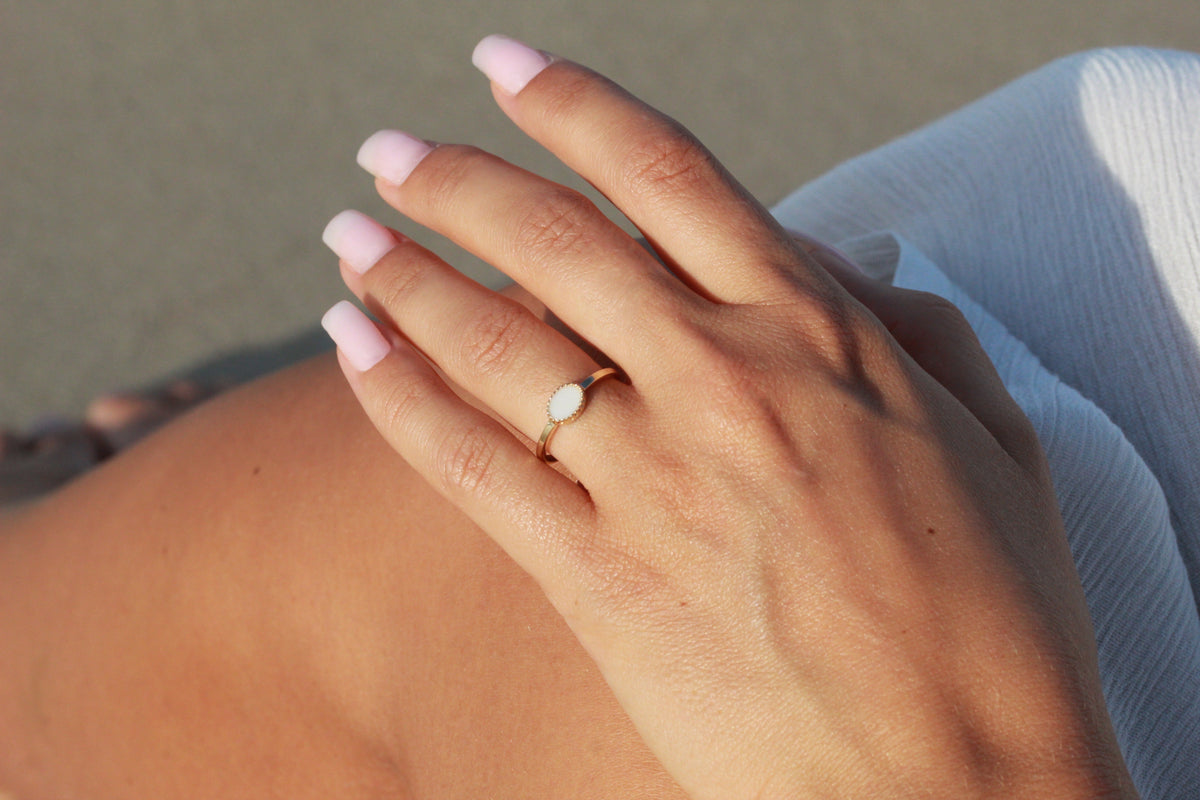 Dunne ring van massief geelgoud met een ovaal vlak van moedermelkhars, gedragen op een hand met lichtroze nagellak.