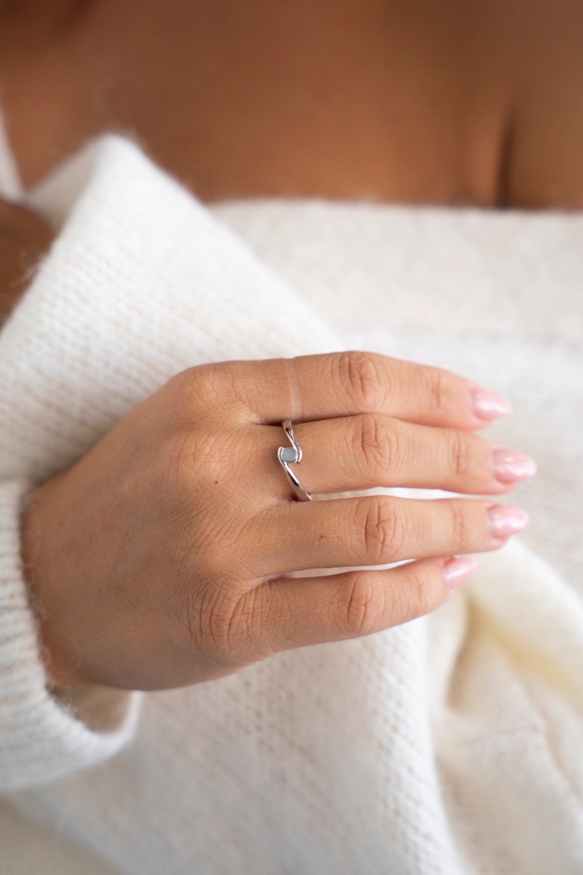 Witgouden Olivia-ring met een kleine moedermelksteen, hand op een witte trui.