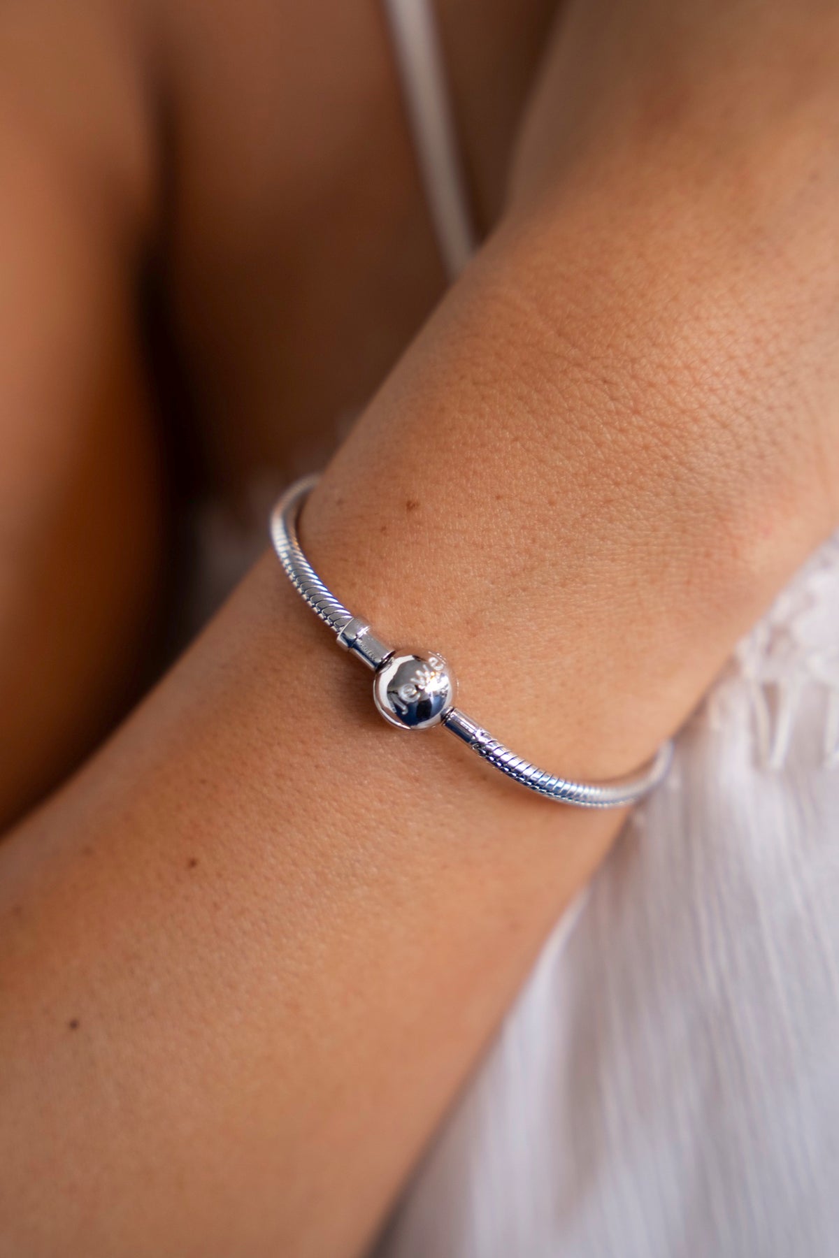 Close-up van de zilveren bedelarmband met slangenschakel en ronde sluiting om de pols.