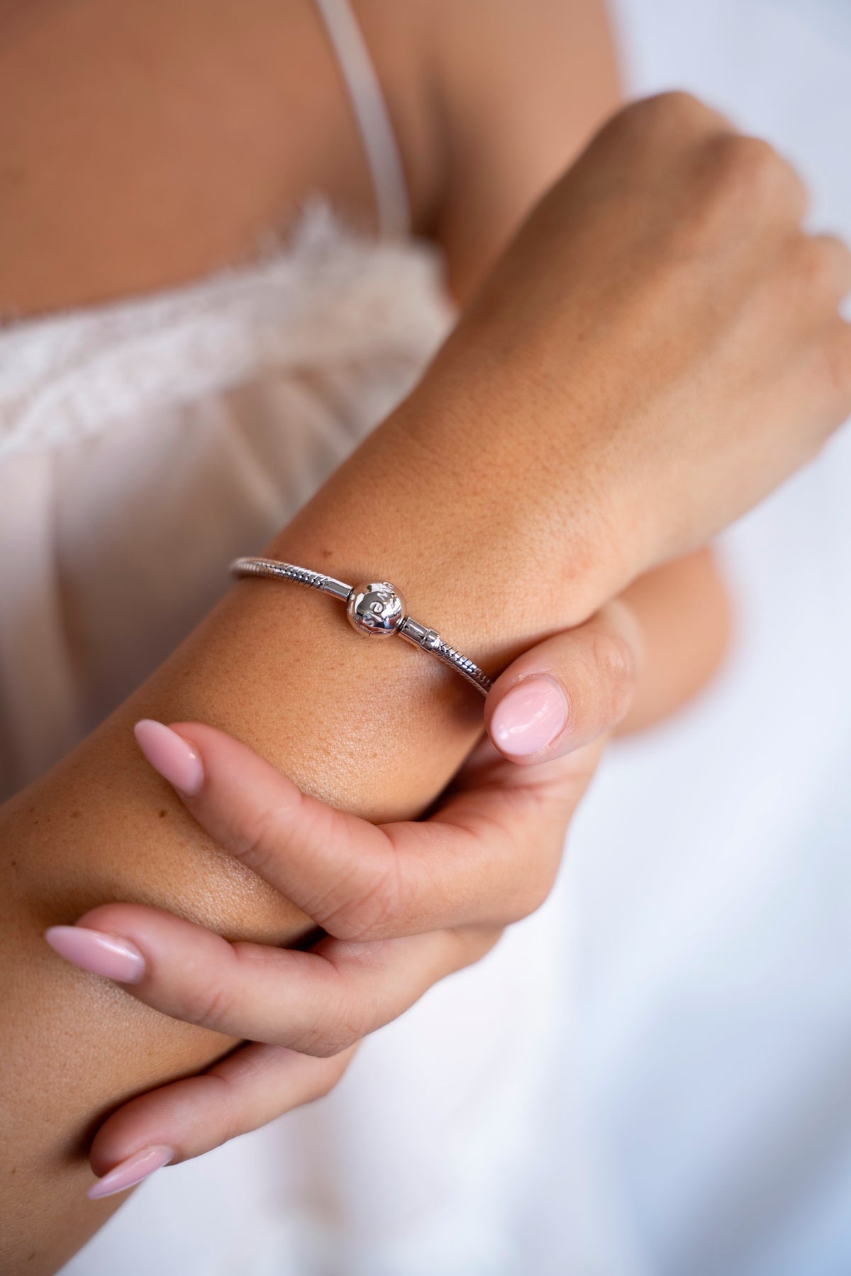 Zilveren bedelarmband van 925 zilver om de pols, de andere hand houdt de arm vast.